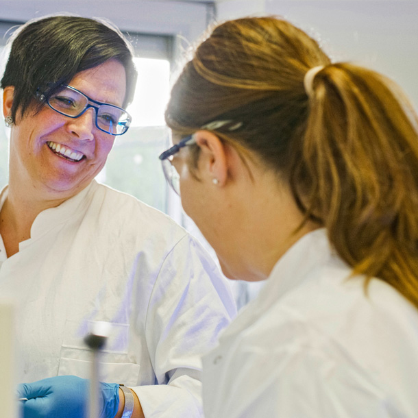 zwei Labor-Mitarbeiterinnen mit Laborkitteln lachen